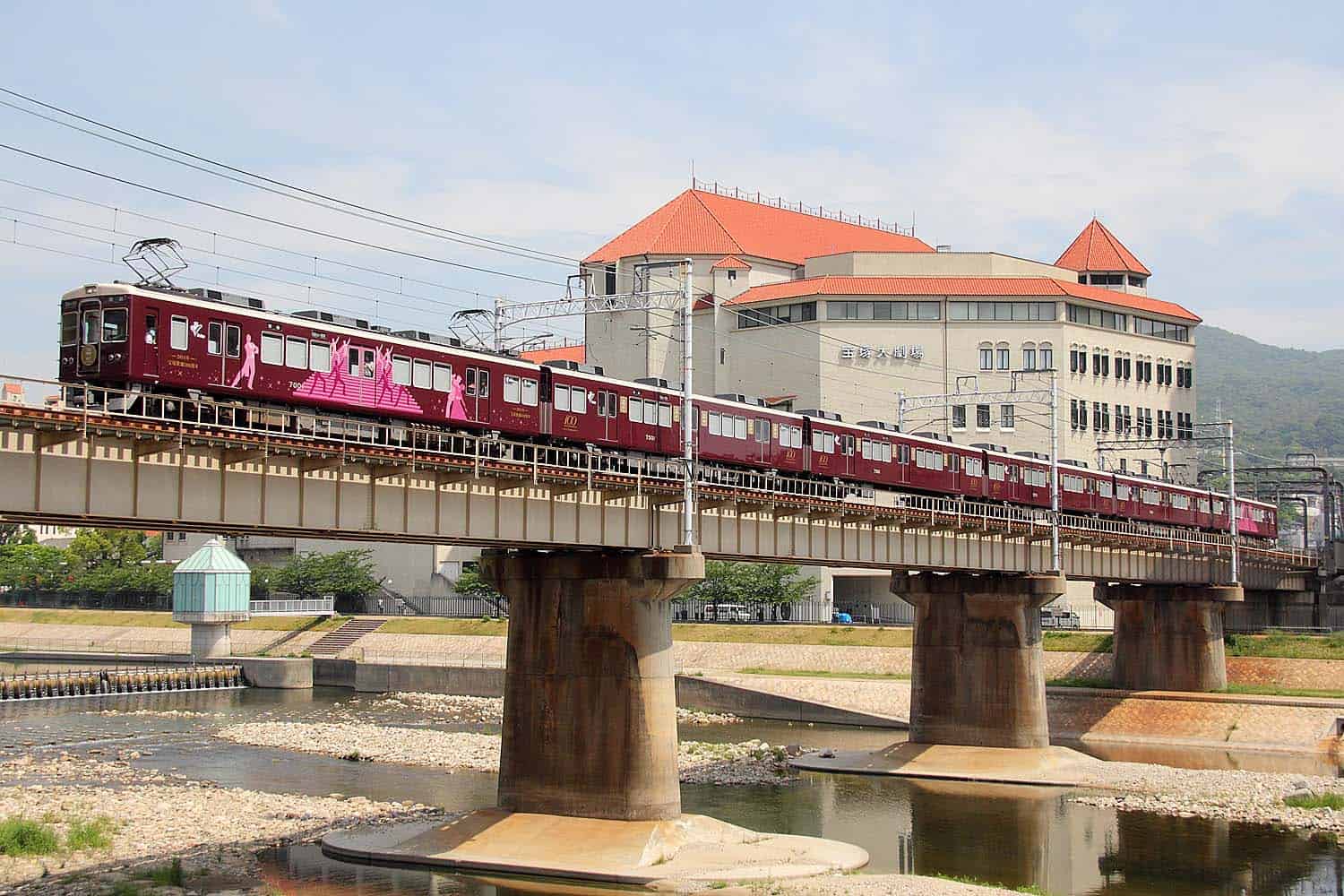 รถไฟฮันคิวที่วิ่งข้ามแม่น้ำมุโกะโดยมีฉากหลังเป็นโรงละครทาคาระซึกะ (Takarazuka)